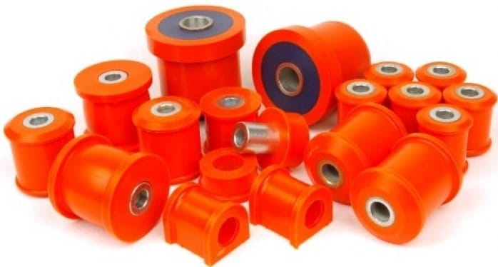 An assortment of orange polyurethane bushes of various sizes, some with metal sleeves, scattered on a white background.
