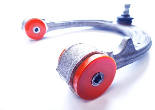 A close-up image of a silver and red car suspension arm and bushing isolated on a white background.