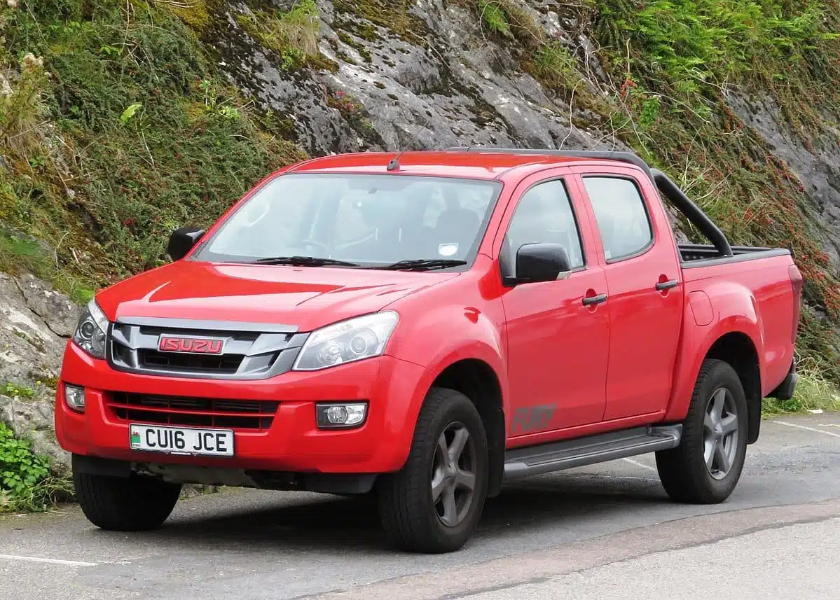 A red Isuzu D-Max pick-up truck parked on a road near a rocky hillside, featuring a clean exterior and visible number plate "cu16 jce".