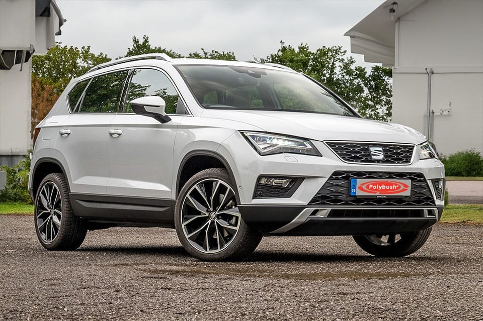A white Seat Ateca SUV parked on a grey pavement, featuring sleek black trim and large alloy wheels, set against a backdrop of green trees and a cloudy sky.(Note: There is no need for translation in this text as, in this case, the same terms are used in both American and British English.)
