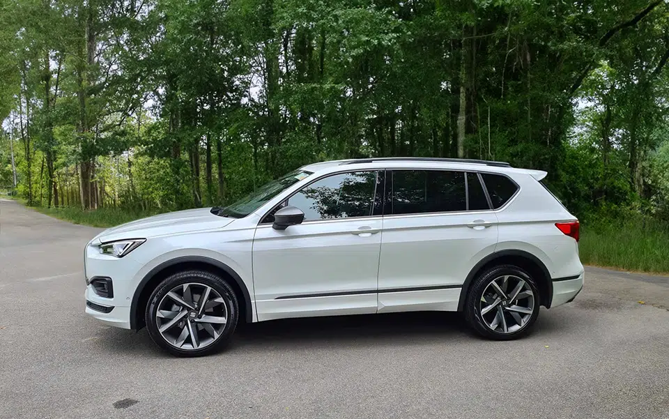 A white 4x4 parked on the side of a road with lush green trees in the background under a clear sky.