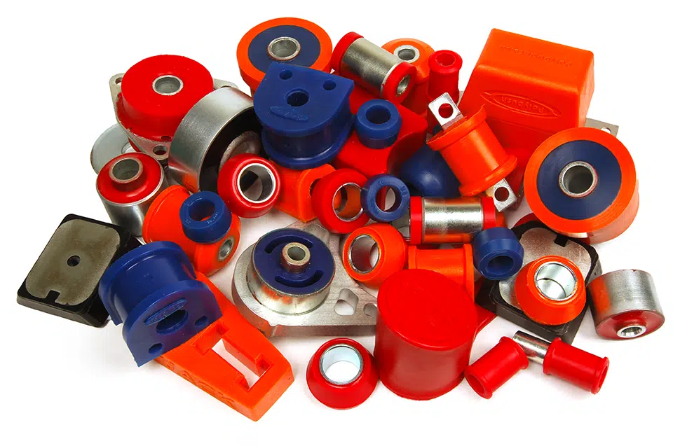 Product Photographs 017 - Edited - Web A collection of colourful polyurethane suspension bushings and metal parts, primarily in red, blue, and orange, scattered on a white background.