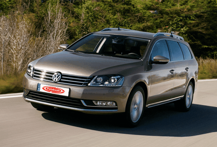 A Volkswagen Passat estate car driving on a sunny road surrounded by lush greenery, showcasing the car's sleek design and roof racks.